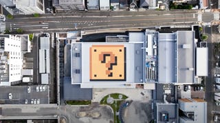 A drone shot from above showing an aerial view of a city street. There's a Mario-esque "?" block on the roof of one of them.